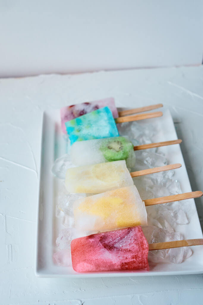 fruit popsicles lines up on a tray in the colors of the rainbow. 