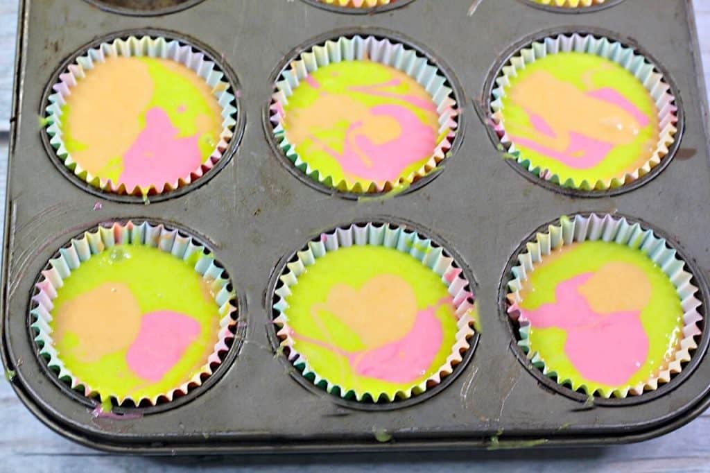 3 colors of cake batter mixed in cupcake tin. 