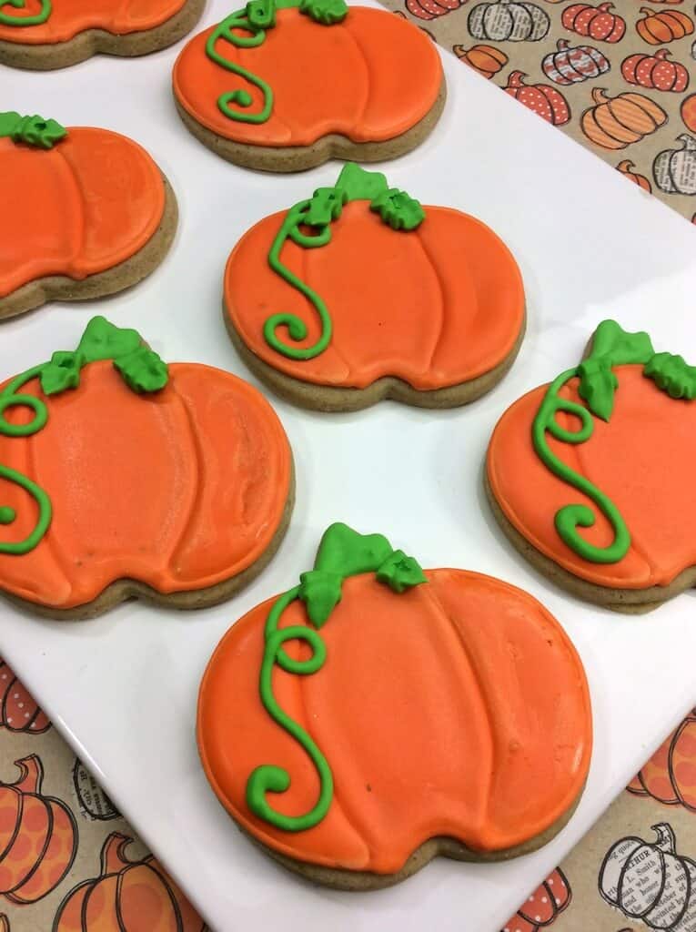 pumpkin spice cookies cut into pumpkin shapes with orange and green frosting 