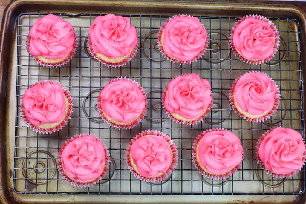 pink grapefruit cupcakes frosted on a cooling tray.