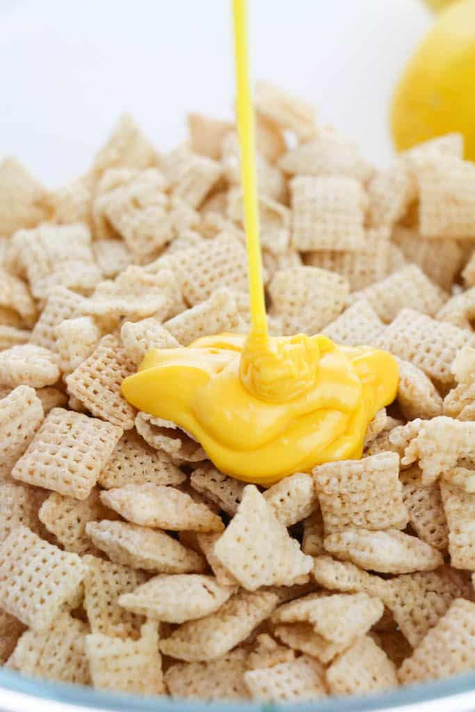 yellow candy melt being poured over Chex cereal.