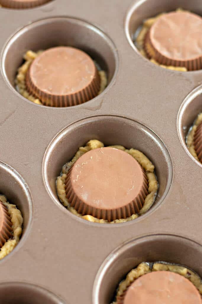 peanut butter cup on top of cookie dough in a muffin tin.