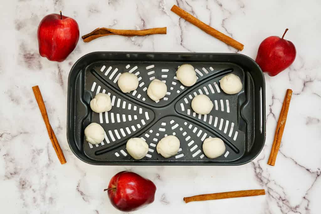 apple donut holes rolled and placed in air fryer basket.