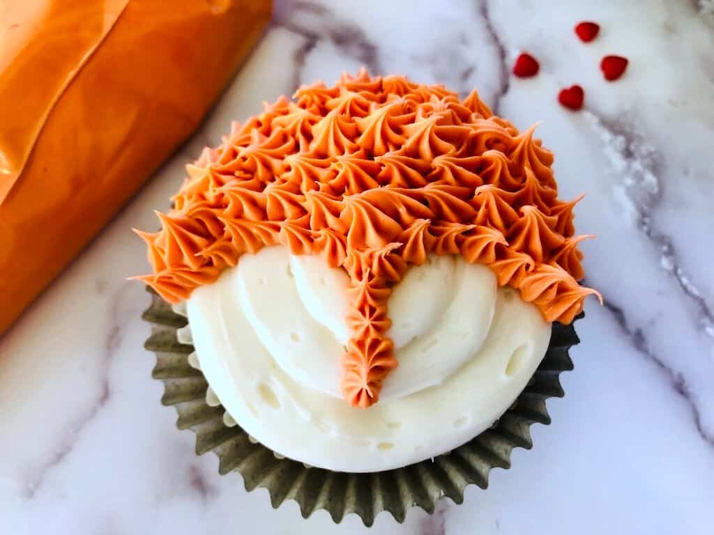 white frosted cupcake with orange star piping at top of fox head.