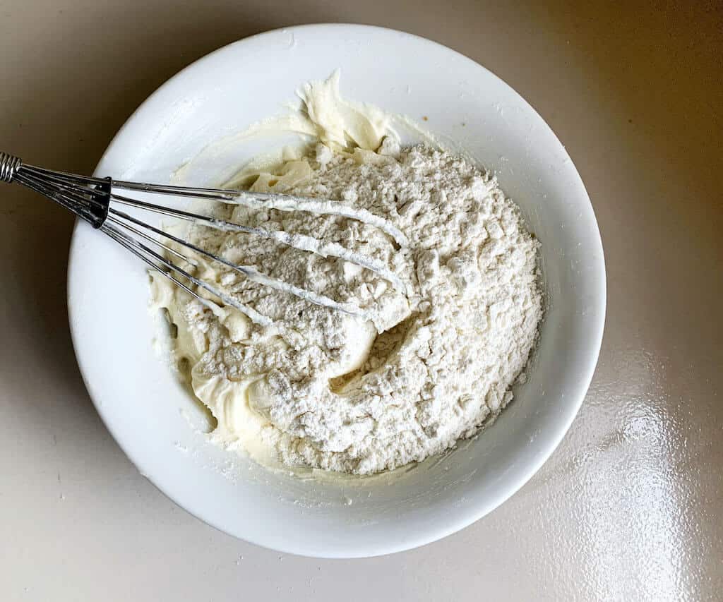 Mixing ingredients with butter in a bowl using hand mixer.