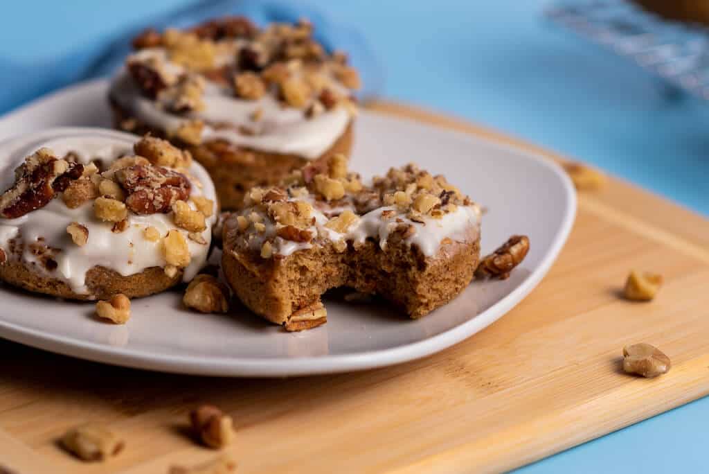 Carrot cake donuts with cream cheese, pecans and walnuts in a plate.