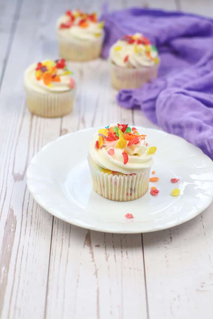 Fruity pebble cupcakes on a white ceramic plate on a wooden table.