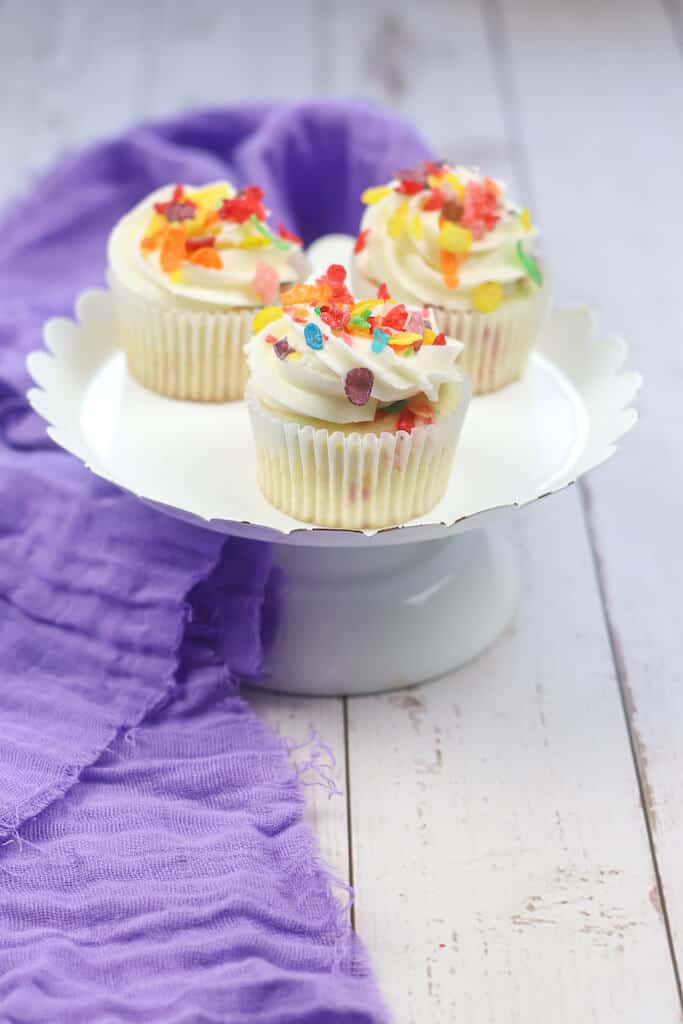 3 Fruity pebble cupcakes on a white disposable plate.